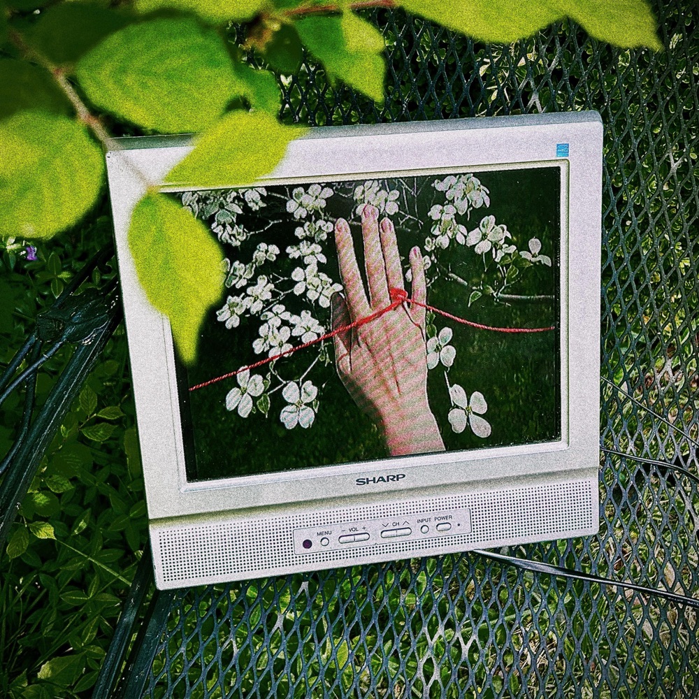 Girls With Boyfriends cover: a silver television on a garden table, showing a hand and a red thread